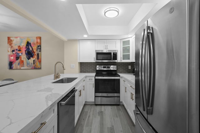 kitchen featuring stainless steel appliances, backsplash, white cabinets, light stone counters, and sink