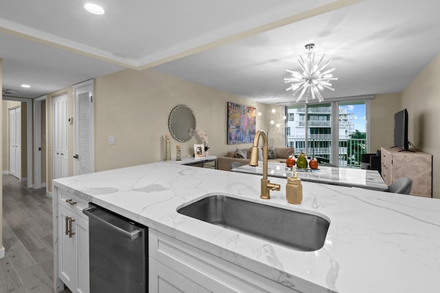 kitchen featuring light wood-type flooring, hanging light fixtures, stainless steel dishwasher, light stone counters, and sink