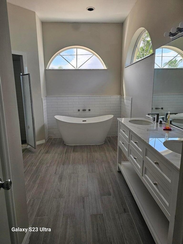 bathroom with vanity, a tub to relax in, wood-type flooring, and tile walls