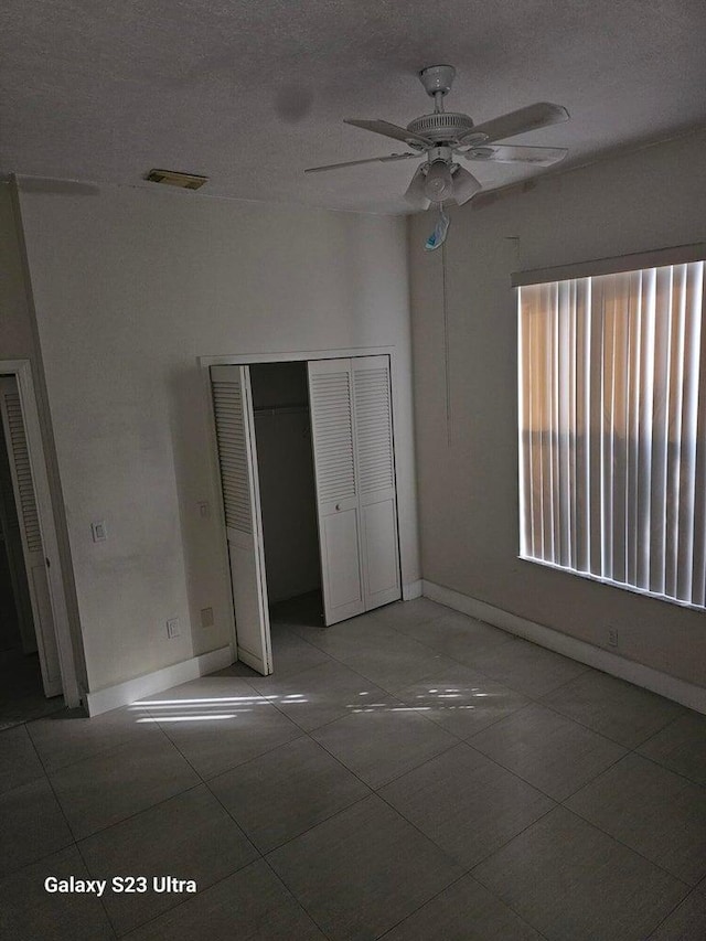 unfurnished bedroom featuring tile patterned flooring, ceiling fan, a closet, and a textured ceiling