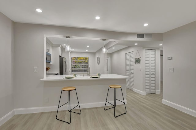 kitchen with stainless steel refrigerator, light hardwood / wood-style floors, white cabinets, a kitchen bar, and kitchen peninsula