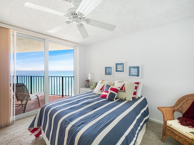 bedroom with ceiling fan, a water view, a textured ceiling, access to exterior, and a wall of windows