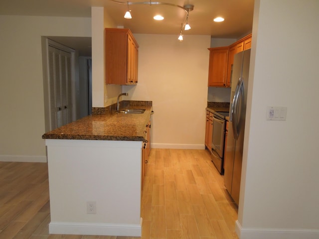 kitchen featuring sink, dark stone counters, light hardwood / wood-style floors, and appliances with stainless steel finishes