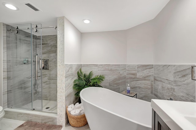 full bathroom with tile walls, vanity, and separate shower and tub