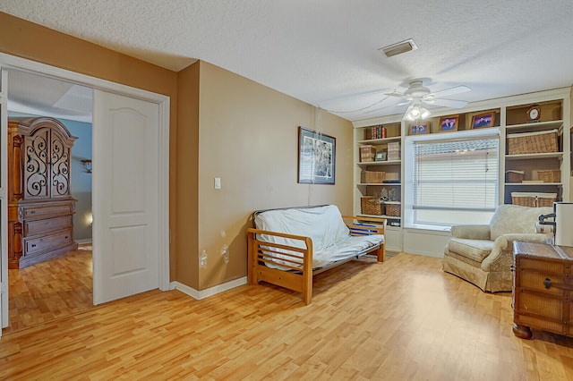 living area featuring built in shelves, ceiling fan, a textured ceiling, and light wood-type flooring