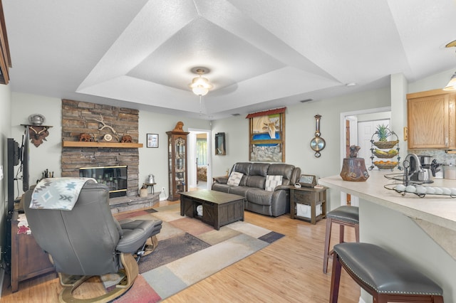 living room featuring a stone fireplace, a raised ceiling, light hardwood / wood-style flooring, and a textured ceiling