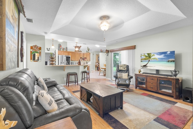 living room with light wood-type flooring, vaulted ceiling, a textured ceiling, and a tray ceiling