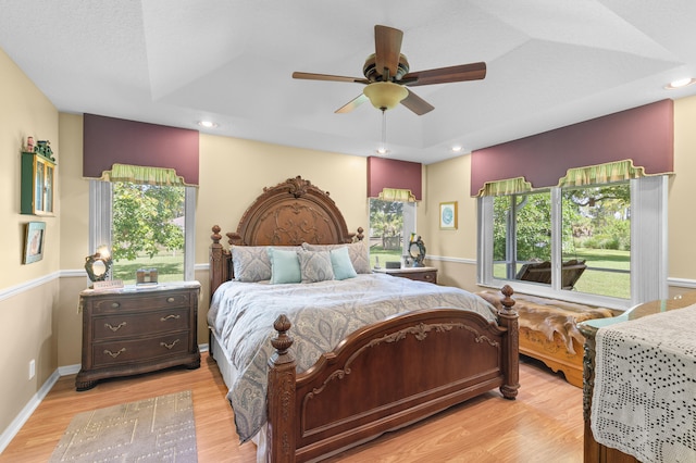 bedroom with light wood-type flooring, ceiling fan, and a raised ceiling