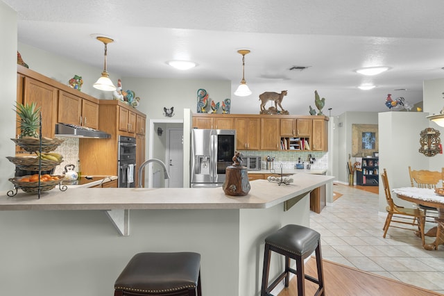 kitchen featuring pendant lighting, a kitchen bar, double oven, tasteful backsplash, and stainless steel fridge