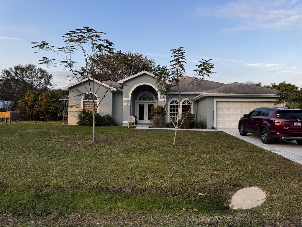 ranch-style house featuring a front yard, a garage, and french doors