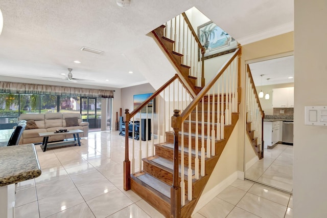 staircase featuring ornamental molding, tile patterned floors, ceiling fan, and a textured ceiling