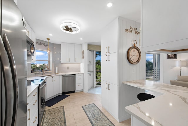 kitchen featuring appliances with stainless steel finishes, white cabinetry, sink, decorative light fixtures, and backsplash