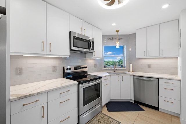 kitchen with white cabinets, appliances with stainless steel finishes, decorative backsplash, sink, and hanging light fixtures