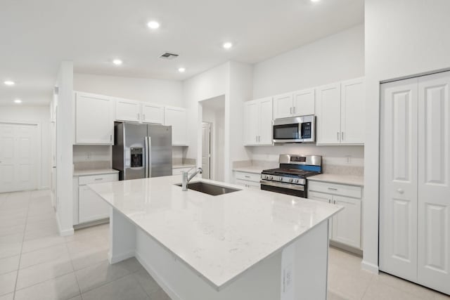 kitchen with sink, appliances with stainless steel finishes, light stone countertops, a kitchen island with sink, and white cabinets