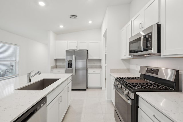 kitchen with sink, stainless steel appliances, light stone countertops, white cabinets, and vaulted ceiling