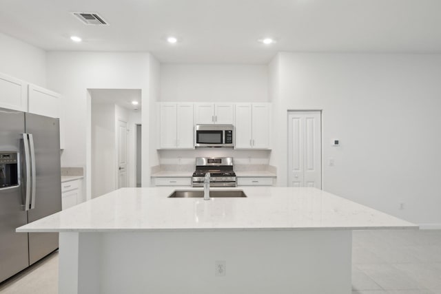 kitchen with light stone counters, appliances with stainless steel finishes, and an island with sink