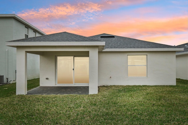 back house at dusk featuring a lawn and a patio