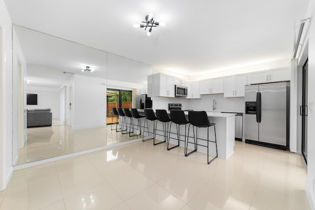 kitchen with a breakfast bar area, white cabinetry, stainless steel appliances, a kitchen island, and light tile patterned flooring