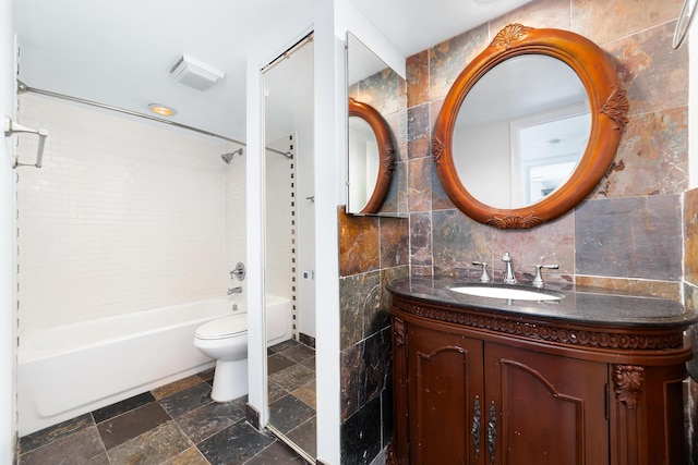 full bathroom with toilet, tiled shower / bath, tile walls, vanity, and backsplash