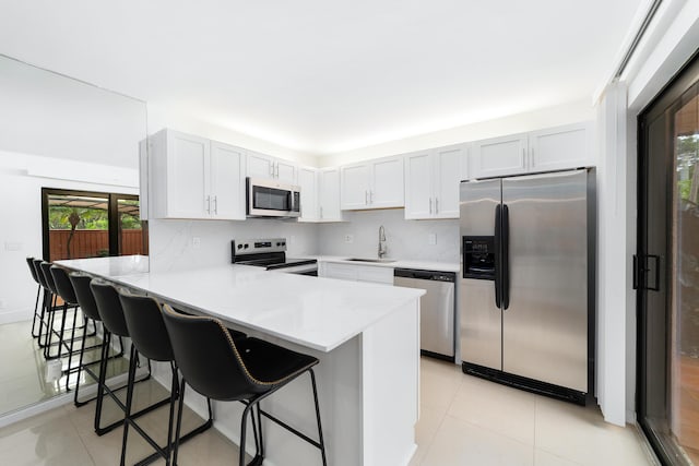 kitchen with appliances with stainless steel finishes, sink, light tile patterned floors, and a kitchen bar