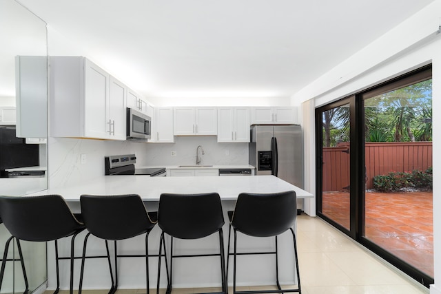 kitchen with appliances with stainless steel finishes, a breakfast bar area, white cabinets, backsplash, and light tile patterned floors