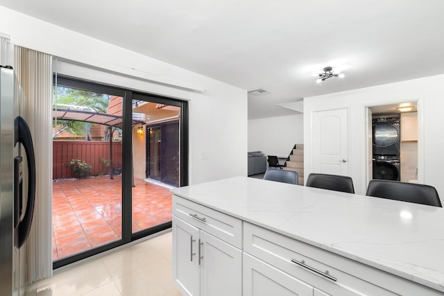 kitchen with stacked washer and dryer, light tile patterned floors, light stone counters, white cabinets, and stainless steel fridge with ice dispenser