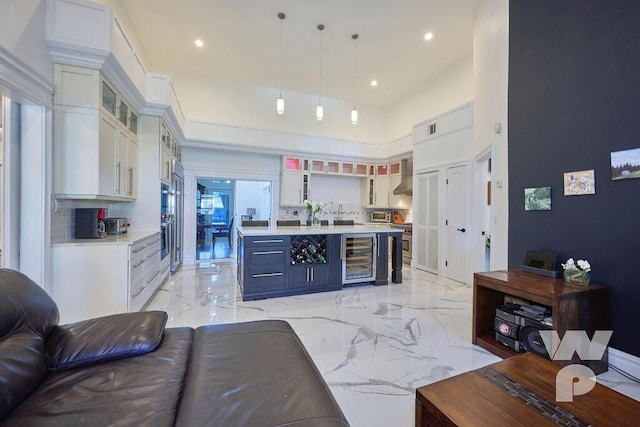 kitchen featuring white cabinetry, wall chimney exhaust hood, beverage cooler, and hanging light fixtures