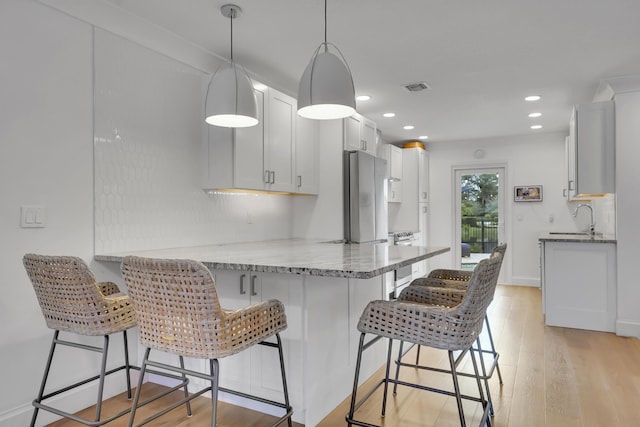 kitchen with sink, stainless steel refrigerator, white cabinetry, decorative light fixtures, and kitchen peninsula