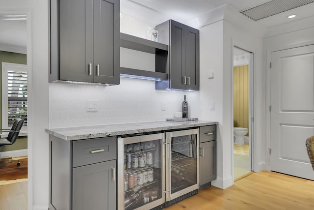 bar featuring gray cabinetry, tasteful backsplash, beverage cooler, light stone countertops, and light hardwood / wood-style floors