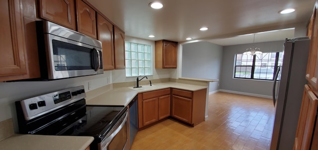 kitchen featuring kitchen peninsula, stainless steel appliances, hanging light fixtures, light hardwood / wood-style flooring, and sink