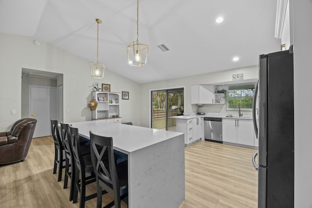 kitchen with vaulted ceiling, decorative light fixtures, white cabinets, a kitchen bar, and stainless steel appliances