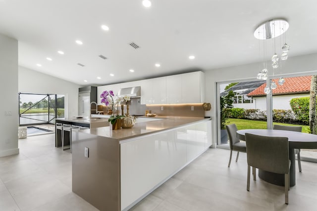 kitchen featuring lofted ceiling, wall chimney exhaust hood, tasteful backsplash, hanging light fixtures, and white cabinets