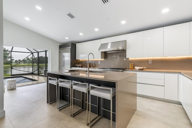 kitchen featuring an island with sink, sink, white cabinets, a kitchen bar, and exhaust hood