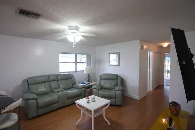 living room featuring ceiling fan, a textured ceiling, and wood-type flooring