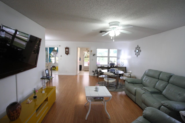 living room with light hardwood / wood-style floors, a textured ceiling, and ceiling fan