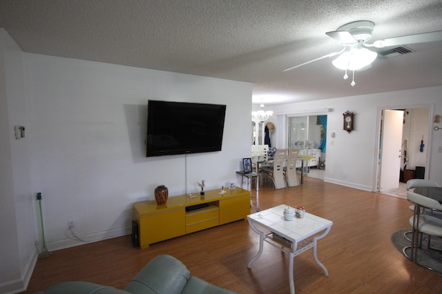 living room featuring ceiling fan with notable chandelier, wood-type flooring, and a textured ceiling