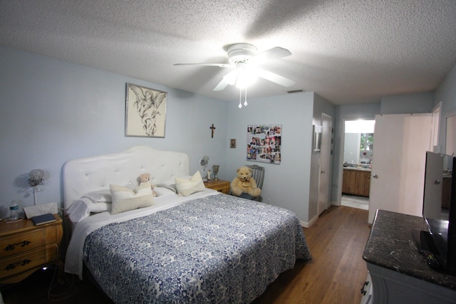 bedroom with a textured ceiling, dark hardwood / wood-style floors, ceiling fan, and connected bathroom