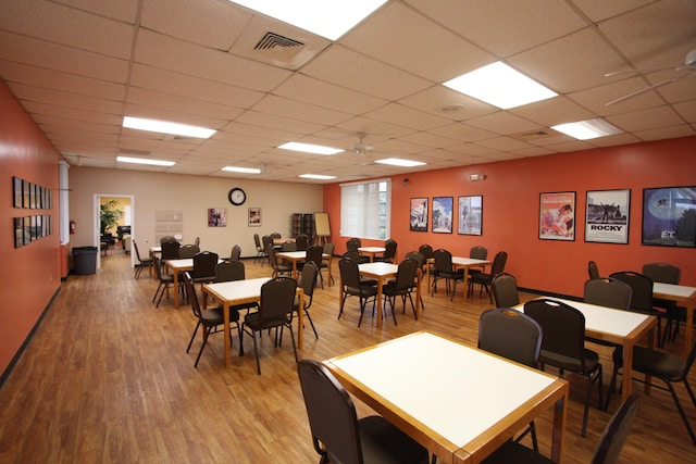 dining area featuring wood-type flooring, a drop ceiling, and ceiling fan