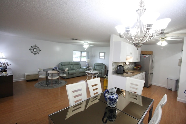 dining space with sink, ceiling fan with notable chandelier, a textured ceiling, and dark hardwood / wood-style flooring