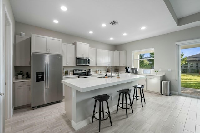 kitchen with a kitchen bar, appliances with stainless steel finishes, a kitchen island with sink, sink, and white cabinets