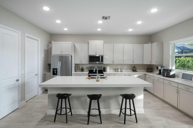 kitchen featuring a kitchen breakfast bar, a kitchen island with sink, white cabinetry, and stainless steel appliances