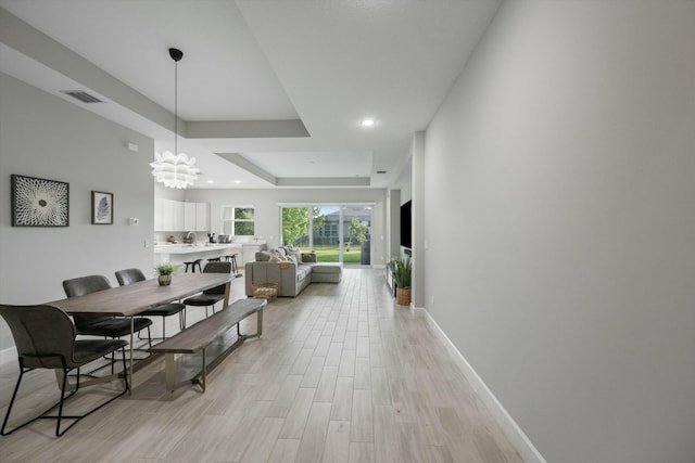 dining area with a tray ceiling, a chandelier, and light wood-type flooring