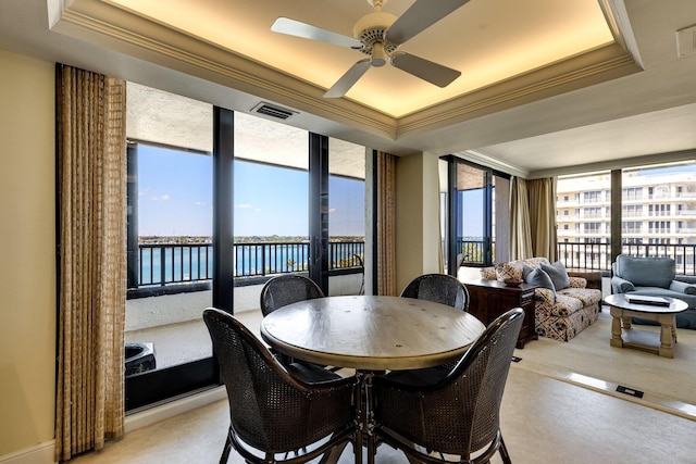 dining area featuring crown molding, a water view, a healthy amount of sunlight, and a tray ceiling