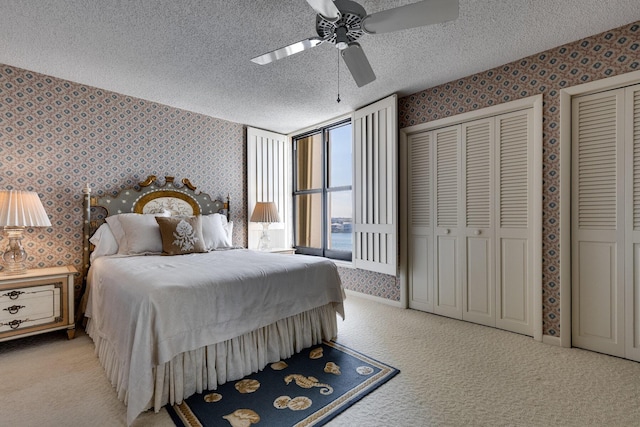 bedroom with multiple closets, light colored carpet, a textured ceiling, and ceiling fan