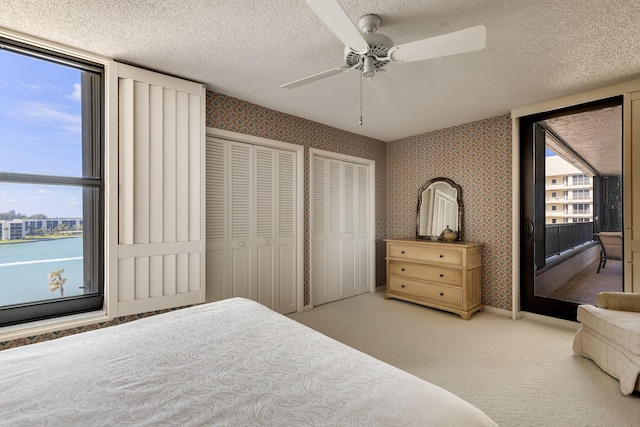 carpeted bedroom with multiple closets, a textured ceiling, and ceiling fan