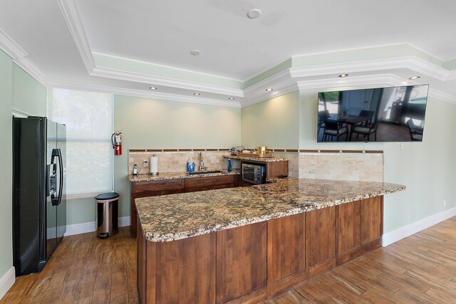 kitchen featuring ornamental molding, stone countertops, black fridge with ice dispenser, and kitchen peninsula