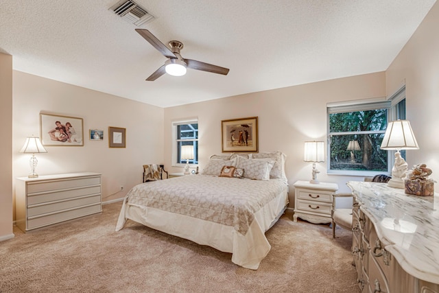 bedroom with ceiling fan, light colored carpet, and a textured ceiling