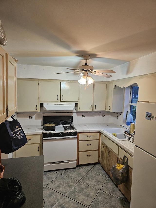 kitchen with sink, cream cabinetry, dark tile patterned floors, and white appliances