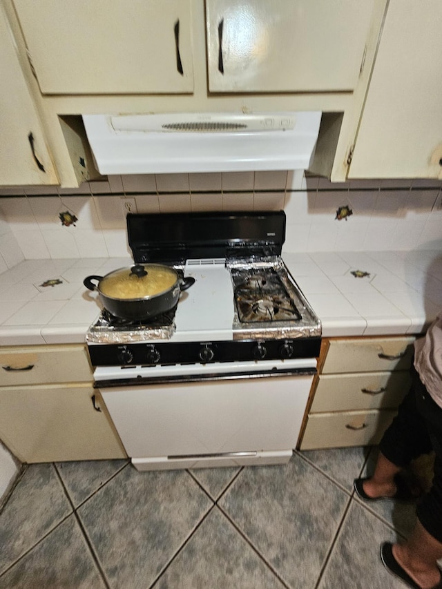 kitchen featuring decorative backsplash, cream cabinetry, extractor fan, and tile patterned flooring