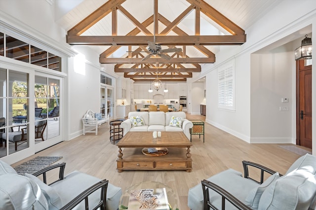 living room with a wealth of natural light, light hardwood / wood-style flooring, high vaulted ceiling, and ceiling fan with notable chandelier